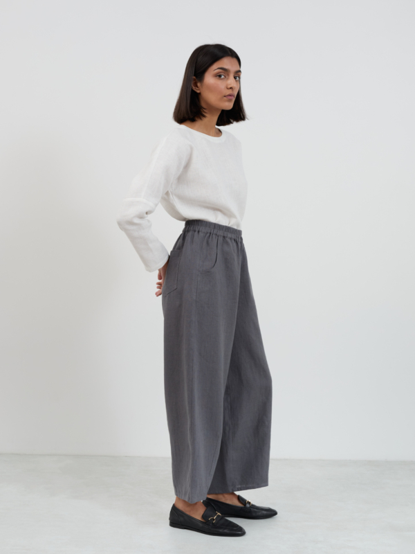 Side view of Haven linen barrel leg pants in charcoal showing the full silhouette, elasticated waist, front side-seam pocket, and wide leg drape to the ankle
