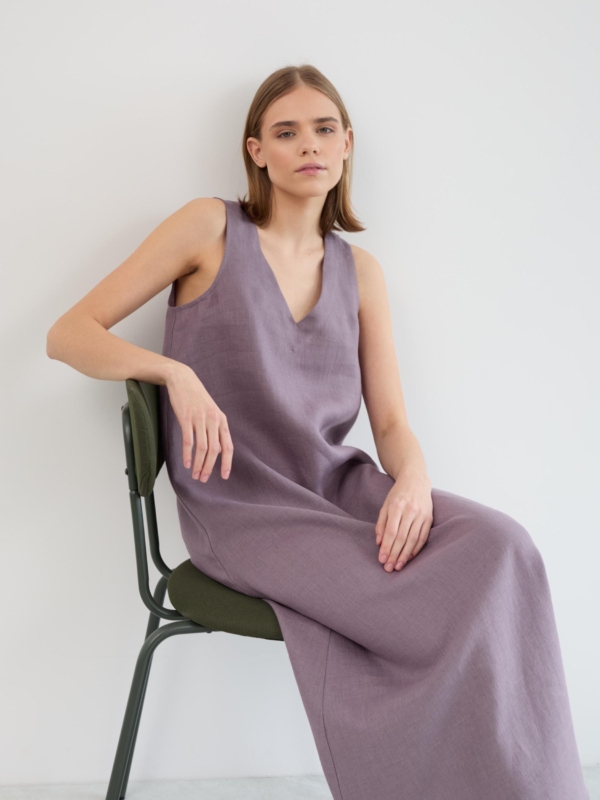 Model seated on a chair wearing the Lanav sleeveless linen maxi dress in lavender violet, showing the V neckline and relaxed drape of the skirt