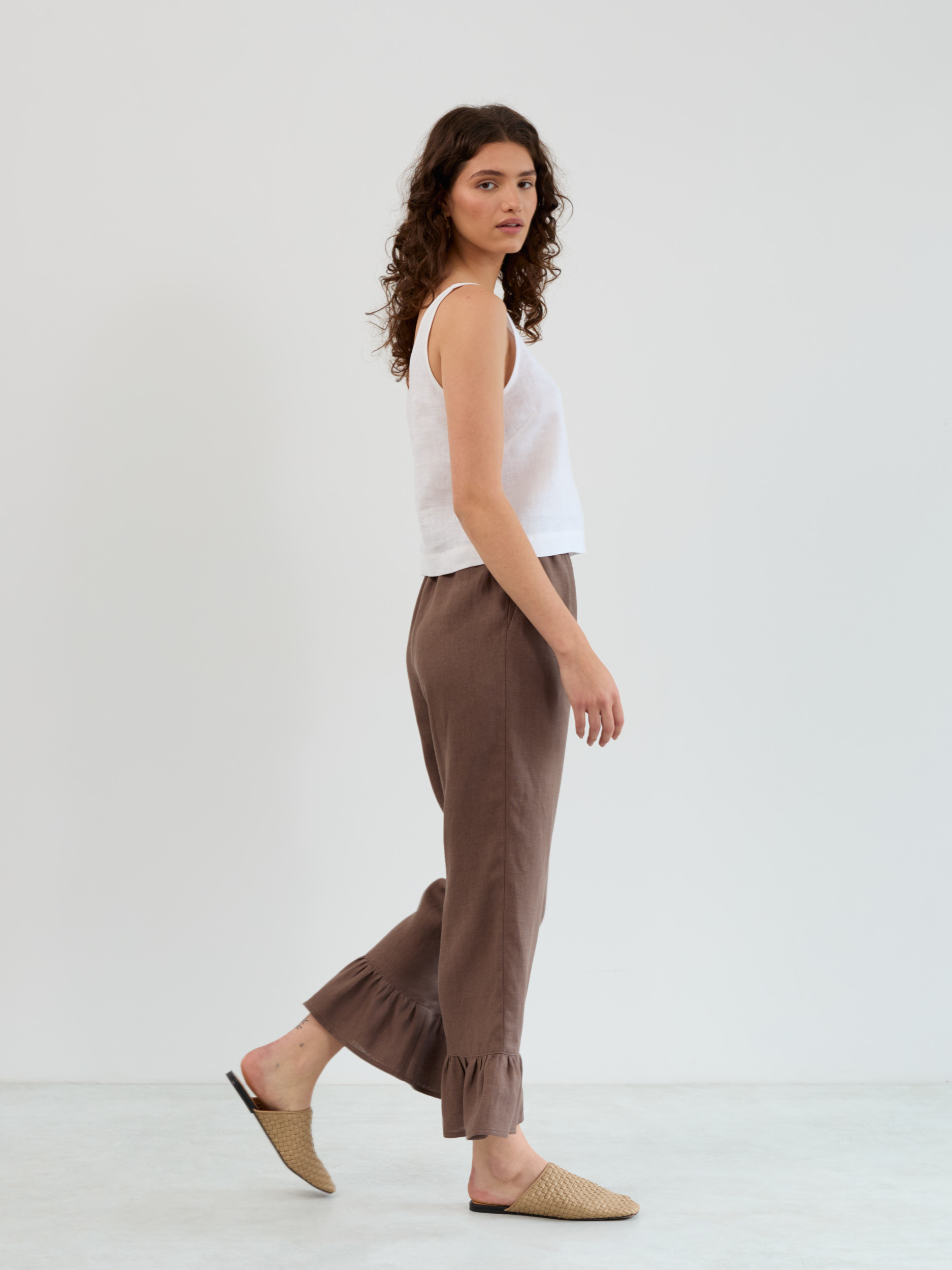 Side walking view of the Gigi linen ruffle pants in cocoa showing the straight leg and gathered flounce at the ankle